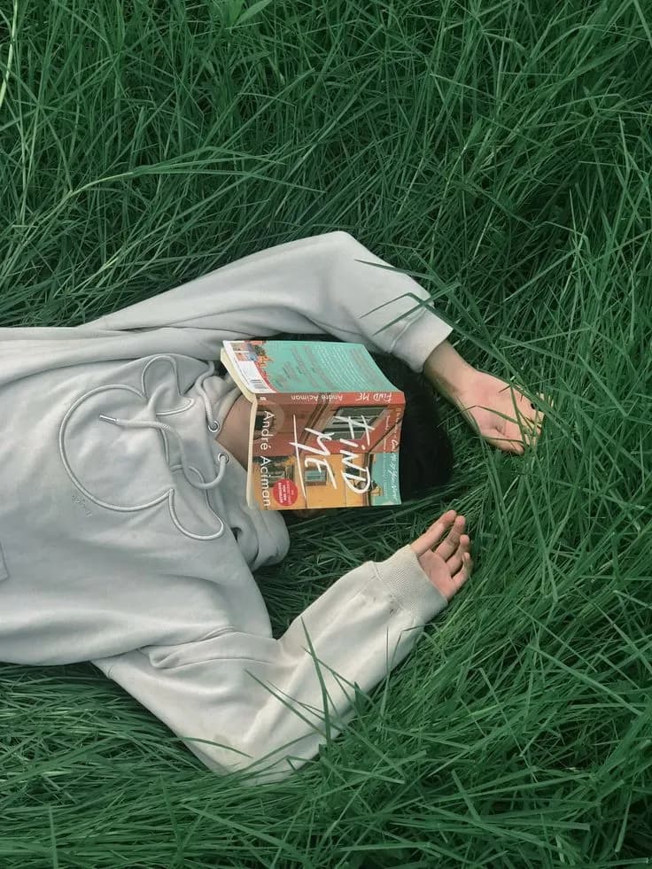 Person resting in tall grass with a book over their face