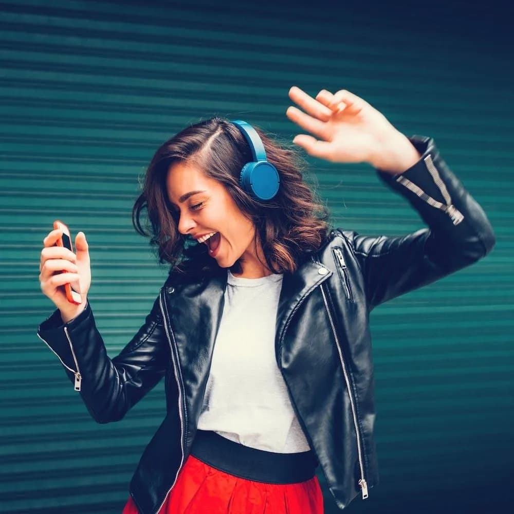 Woman with blue headphones dancing to music on her phone